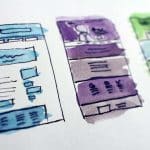 Hand-drawn webpage wireframe sketches with blue, purple, and green markers on a white paper, illustrating rough designs for a website layout with text placeholders and menu bars.