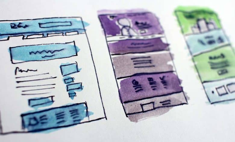 Hand-drawn webpage wireframe sketches with blue, purple, and green markers on a white paper, illustrating rough designs for a website layout with text placeholders and menu bars.
