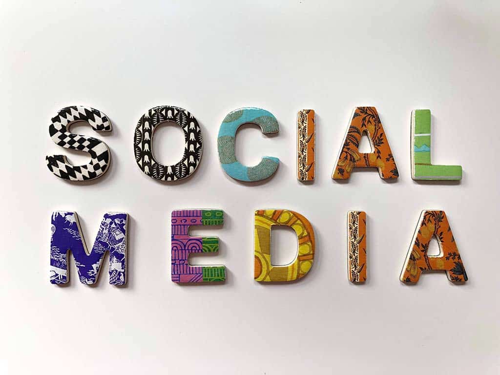 The phrase "social media" is spelled out with colorful, patterned letters, each uniquely designed with different textures and motifs, laid flat on a light grey background.
