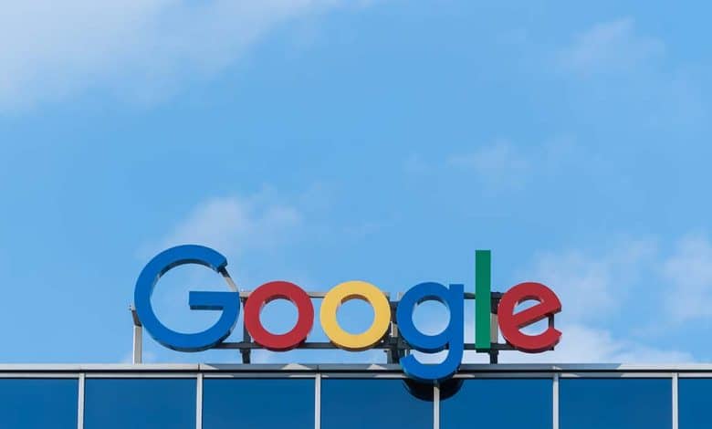 Colorful google logo on top of a building under a blue sky with fluffy clouds. the letters are in bright blue, red, yellow, and green against the building's reflective glass exterior.