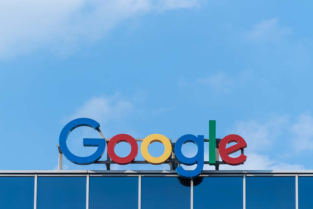 Colorful google logo on top of a building under a blue sky with fluffy clouds. the letters are in bright blue, red, yellow, and green against the building's reflective glass exterior.
