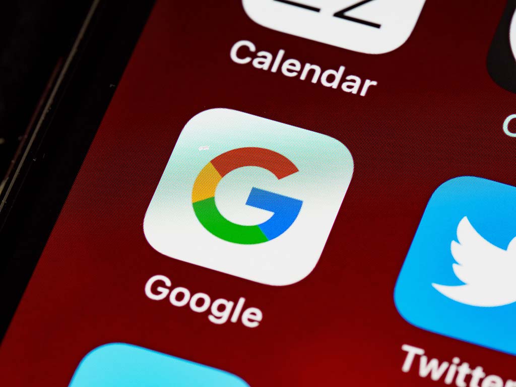Close-up view of a smartphone screen displaying app icons, with a focus on the google app icon. the icon features google’s signature colorful letter "g". surrounding icons include the calendar and twitter apps.