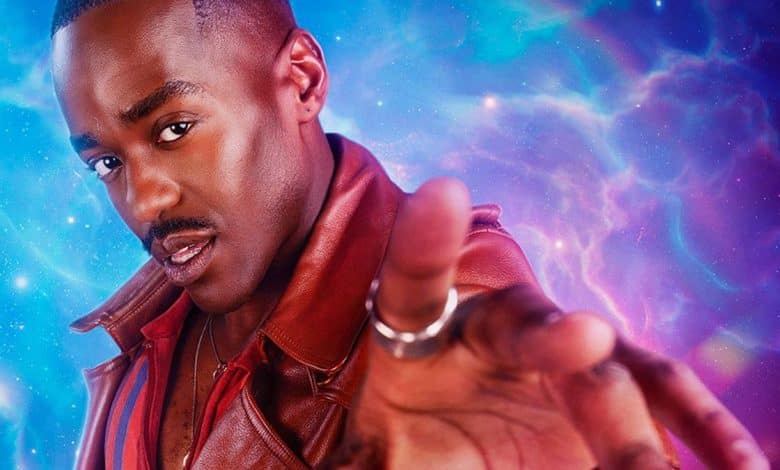 A man with a dark complexion, wearing a red leather jacket, extends his hand towards the camera against a vibrant cosmic backdrop with pink and blue nebulae. His expression is intense and focused. This