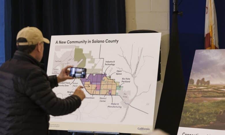 A person points at a large map titled "a new community in Solano County" during a presentation. The map displays various zones like residential, industrial, and open space. A California flag is visible