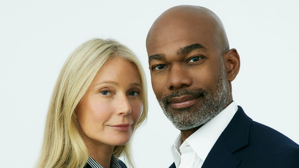 A professional portrait of a white woman and a black man close together, both smiling subtly. The woman has long blonde hair and is wearing a light blazer, while Dr. Julius Few has a closely
