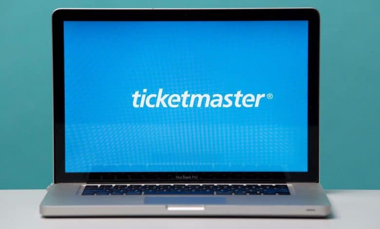 A MacBook Pro laptop open on a desk displaying the Ticketmaster website with a headline about "California Bill Targets Ticketmaster's Fair Play" on its screen, set against a bold blue background and
