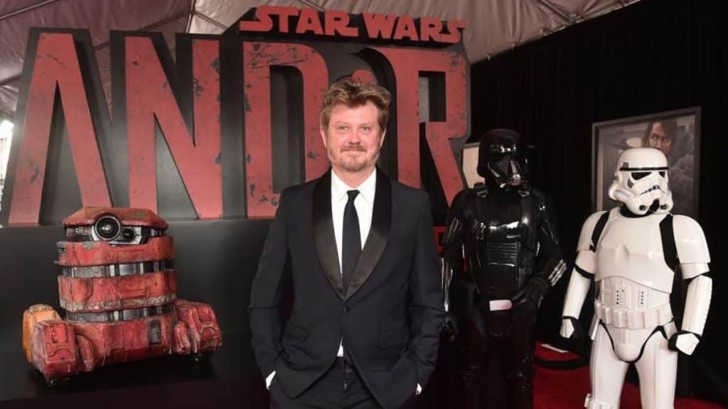 A man in a dark suit stands on the red carpet at the "Andor" premiere, flanked by a stormtrooper and a character in red armor, with the large "Andor