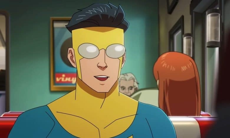 A scene from an animated series showing a young male superhero with yellow goggles, spikey dark hair, wearing a blue and yellow suit, seated, and looking slightly surprised in a room with green
