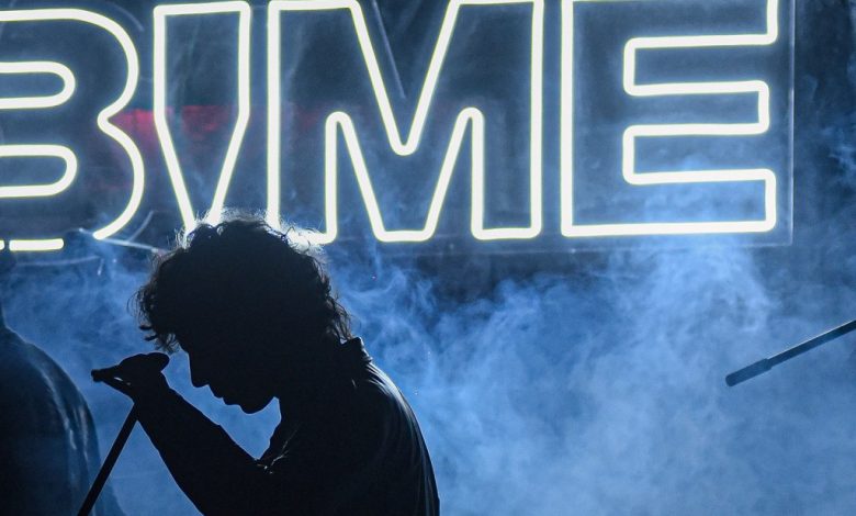 Silhouetted figure of a person singing into a microphone on a foggy stage, with a bright neon sign that reads "BIME Bogotá 2024" in the background, creating