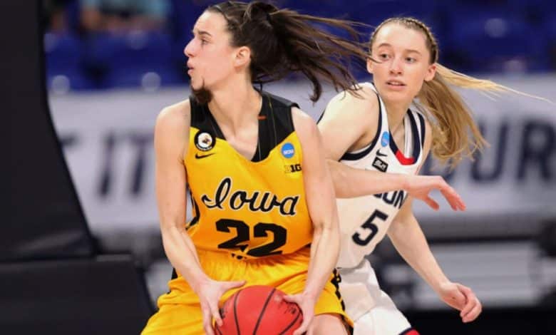 Two female basketball players in motion during a game. The player in a yellow Iowa jersey, number 22, dribbles the ball, while a player in a white UConn jersey from a rival team