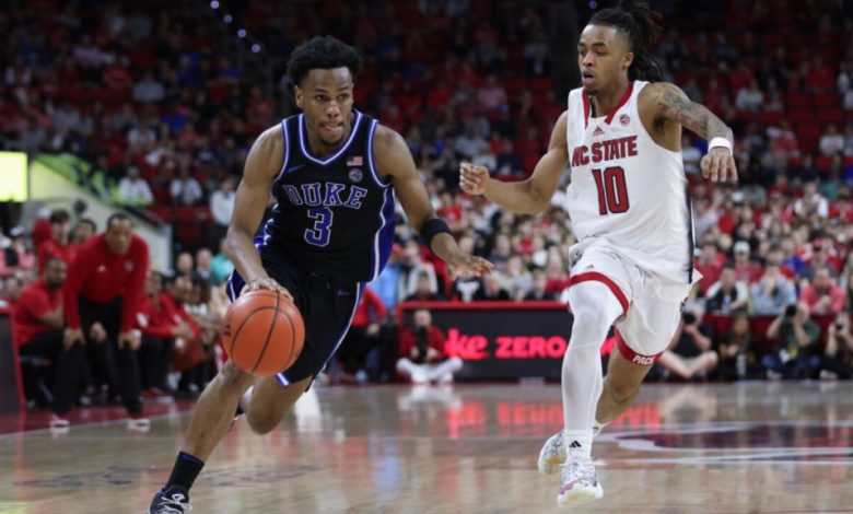 Two college basketball players in action during the 2024 NCAA Elite Eight game. A Duke player in a blue uniform, number 3, dribbles the ball quickly past an N.C. State player