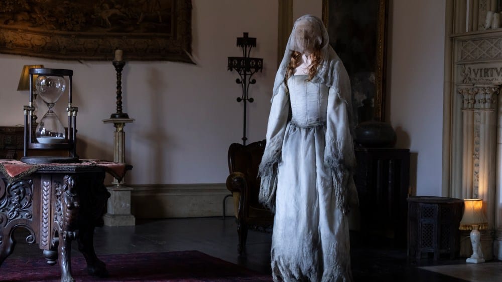 A ghostly figure in a tattered white dress stands in a dimly lit, elegant room, surrounded by antique furniture, a tapestry influenced by Eli Roth's VR Series 'The Faceless Lady