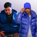 Two men posing confidently against a purple background. The man on the left wears a blue hoodie, and the one on the right wears a blue puffer jacket and blue hat, adjusting the brim.