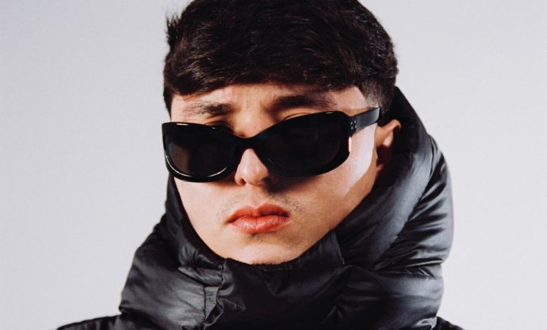 A young man wearing oversized black sunglasses and a glossy black puffer jacket looks directly at the camera with a neutral expression, against a plain light background, in the promotional materials for the 2024 U