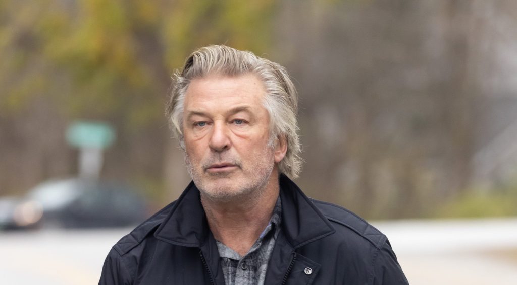 A middle-aged man with graying hair and a serious expression walks outdoors, wearing a black jacket. Trees with autumn leaves in the background suggest a cool, overcast day ahead of the 'Rust