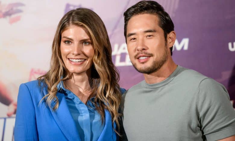 A man and a woman smiling at an event, standing together against a promotional backdrop for "Quantum Leap." The woman wears a blue blouse, and the man wears a grey t-shirt. Both have