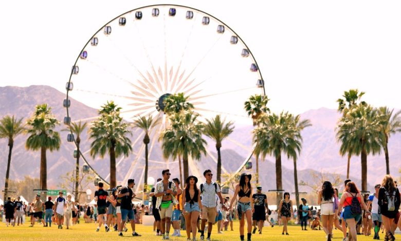 Young adults walk across a grassy area at Coachella 2024 music festival, with a large ferris wheel and palm trees against a mountainous backdrop under a clear sky.