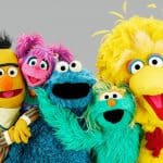 Group of colorful Sesame Street characters including Ernie, Bert, Abby Cadabby, Cookie Monster, Rosita, Big Bird, and Grover posing in support of the WGA strike cheerfully together