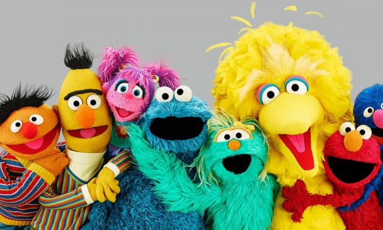 Group of colorful Sesame Street characters including Ernie, Bert, Abby Cadabby, Cookie Monster, Rosita, Big Bird, and Grover posing in support of the WGA strike cheerfully together