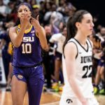 An LSU women's basketball player, number 10, wearing a purple and gold uniform, celebrates on the court with a hand gesture as opponents and spectators surround her in the background during the Elite Eight.