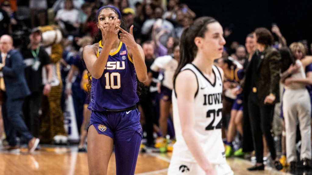 An LSU women's basketball player, number 10, wearing a purple and gold uniform, celebrates on the court with a hand gesture as opponents and spectators surround her in the background during the Elite Eight.