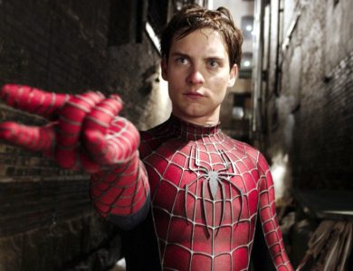 A man dressed as Spider-Man stands in a dark alley, extending his hand forward to mimic shooting a web, with a focused expression on his face. He wears the iconic red and blue Raimi