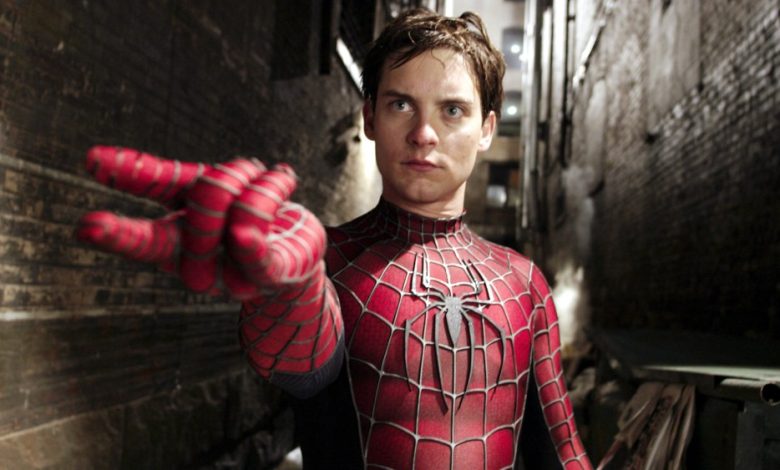 A man dressed as Spider-Man stands in a dark alley, extending his hand forward to mimic shooting a web, with a focused expression on his face. He wears the iconic red and blue Raimi