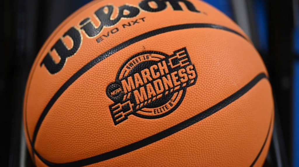 Close-up of an orange wilson basketball embossed with the 2024 Women's NCAA March Madness Elite Eight logo, focus sharp on the text and logo, against a blurred blue background.