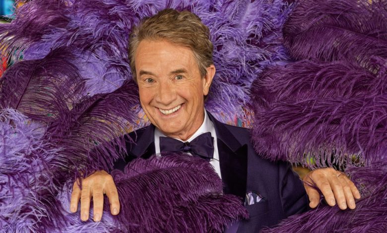 A joyful elderly man, resembling Martin Short, with styled hair and a friendly smile wears a formal blue suit with a matching tie and pocket square. He is surrounded by an array of colorful, fluffy purple