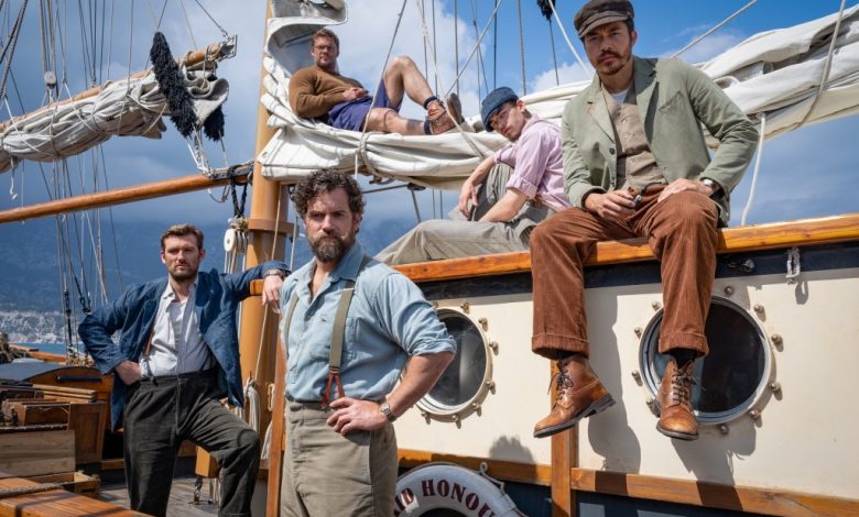 Five actors in vintage nautical attire pose on and beside a classic sailing ship named "Honour." One stands confidently on deck, two sit on the railing, and two lounge in the rigging,