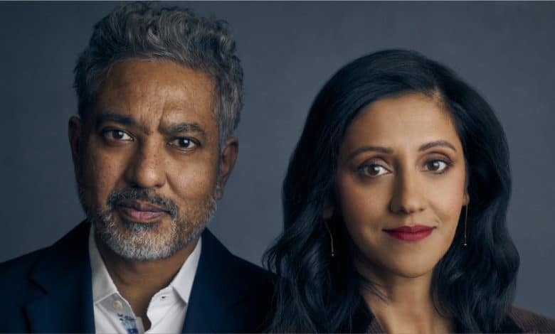 A middle-aged man with graying hair and a woman with long dark hair, both of South Asian descent, stand side by side looking into the camera against a slate backdrop.