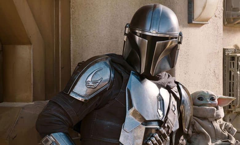 The Mandalorian in full armor stands next to Baby Yoda, who looks up from a pouch. They are surrounded by a desert-like, mechanical backdrop inspired by 'Star Wars' 2026 Disney
