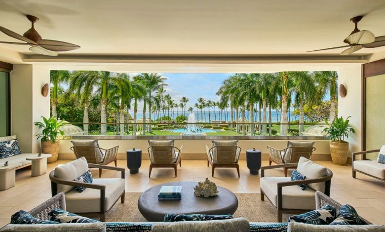 An elegant outdoor living area with comfortable seating overlooking the Grand Wailea Resort, featuring tall palm trees, a large swimming pool, under a clear blue sky.