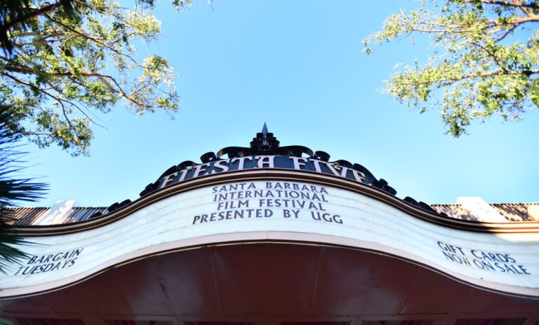 This image shows the top facade of the Fiesta 5 Theater, advertising the Santa Barbara International Film Festival presented by UGG. Blue sky forms the backdrop above the cream-colored, ornate entrance.