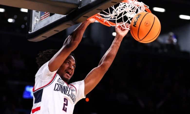 A basketball player in a "Connecticut" jersey, number 2, dunks a basketball into the hoop during a night game at the NCAA Final Four 2024, intense expression on his face