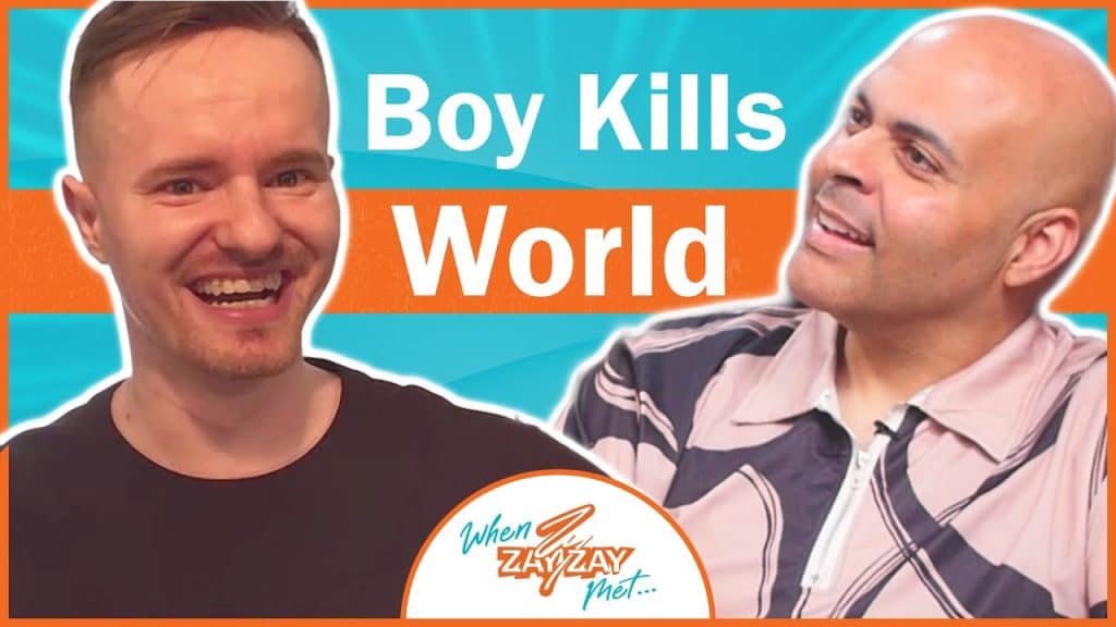 Two men smiling during an interview, one with a short beard and the other bald, framed by a vibrant orange and blue background with the text "boy kills world" and "when zayzay met..." visible.