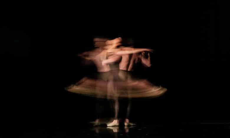 A blurred image of an American Ballet Theatre dancer in mid-twirl on a dark stage, capturing a sense of motion with multiple overlapping silhouettes suggesting rapid spinning.