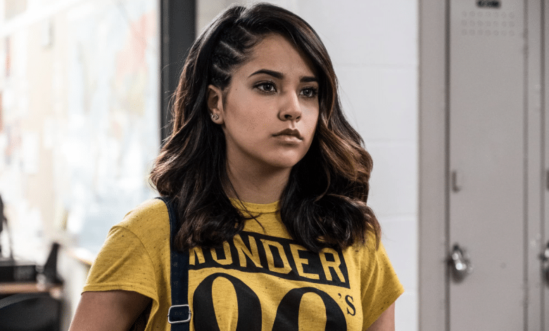 Becky G, with medium-length dark hair styled in braids, looks intensely to the side. She wears a vibrant yellow t-shirt with "thunder" written in black, standing in a