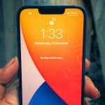 A hand holding an iPhone displaying the lock screen with the time 1:33 and the date "Wednesday, 9 December." The screen background features a vibrant orange and blue gradient. No notifications are