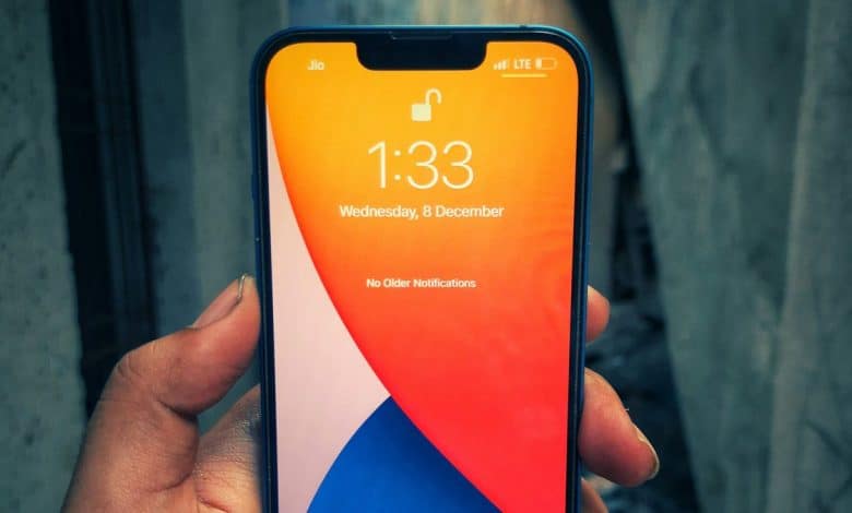 A hand holding an iPhone displaying the lock screen with the time 1:33 and the date "Wednesday, 9 December." The screen background features a vibrant orange and blue gradient. No notifications are