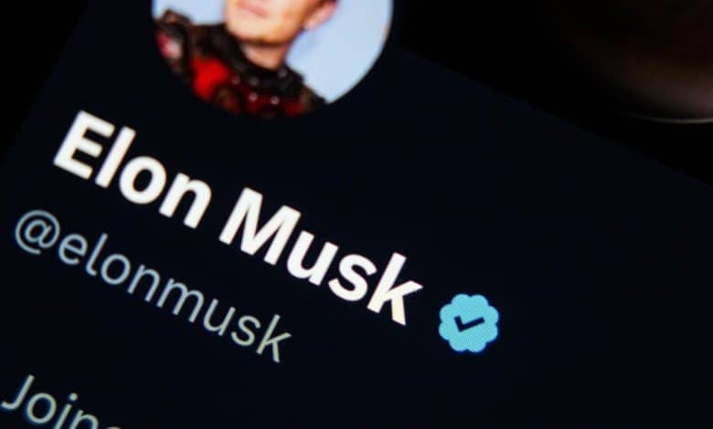 Close-up of a digital screen displaying Elon Musk's Verified X profile with his username @elonmusk and a part of his profile picture showing him in a red outfit.