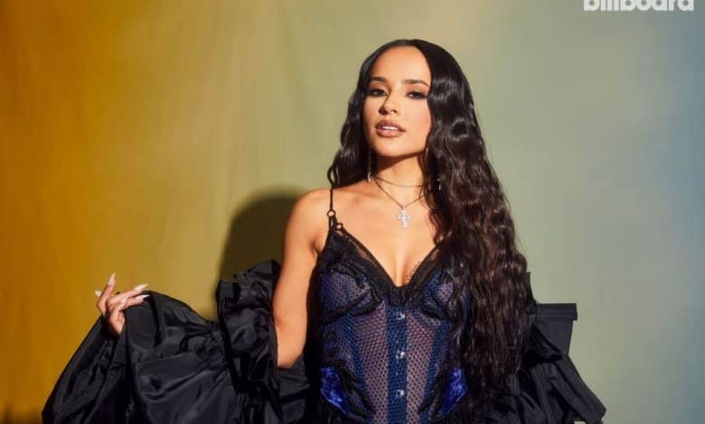 A woman poses confidently in a glamorous navy blue sequined dress with a voluminous black overlay at the Latin AMAs 2024. She accessorizes with a delicate cross pendant. A dual-toned