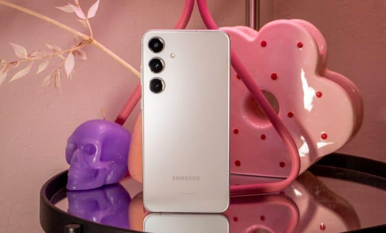 A Samsung smartphone with a white back and triple camera setup rests on a glass surface, surrounded by a pink neon heart light, purple skull, and pink cherry blossoms, illustrating the step-by-step guide