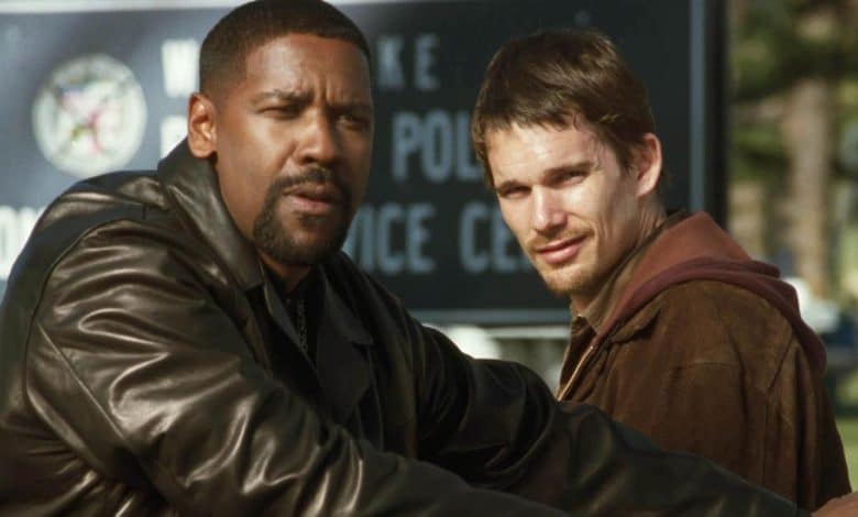 Two men in a park, one african-american in a black leather jacket, the other caucasian in a brown jacket, both looking seriously towards the camera with a police sign in the background.