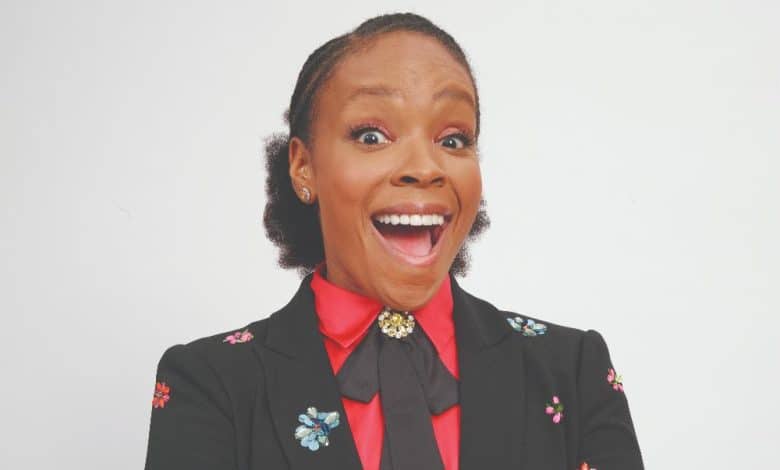 A joyful african american woman with her mouth wide open in excitement, wearing a black blazer with colorful floral embroidery and a red blouse, against a white background.