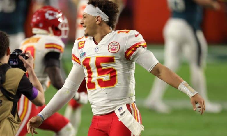 A kansas city chiefs quarterback wearing jersey number 15 celebrates on the football field. he is expressing joy, extending his right arm, while photographers capture the moment, including one in a black jacket on the left.