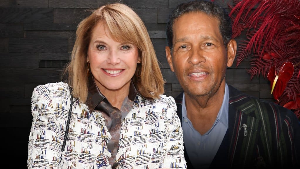 A smiling man and woman pose together in front of a wooden background. The woman, identified as Katie Couric, wears a patterned white blazer, and the man, recognized as Bryant Gumb