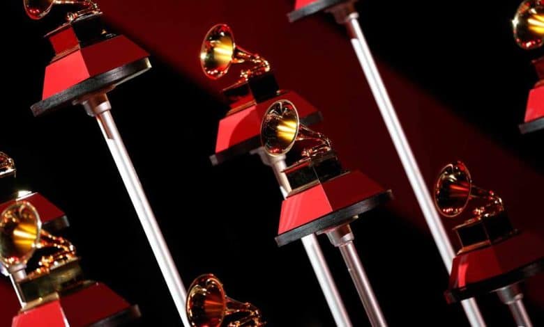 A series of Grammy Awards lined up, featuring the iconic gramophone shape atop a black and red column, set against a dark background. The golden gramophones gleam under the spotlight at the