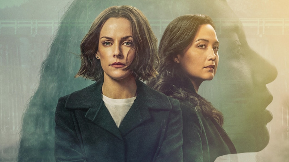 Promotional image for the drama series "Under the Bridge" featuring two women, one with short blonde hair and the other with long brown hair, dressed in dark coats. A shadowy, enigmatic