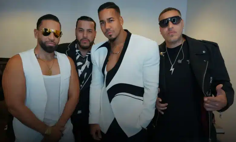 Aventura, Four men stand together for a group photo against a plain background. All are dressed stylishly: three wear black and white outfits, with one in a white blazer with black trim, and the fourth wears an all-black outfit with sunglasses and a lightning bolt necklace, reminiscing on their Aventura Madison Square Garden concert.